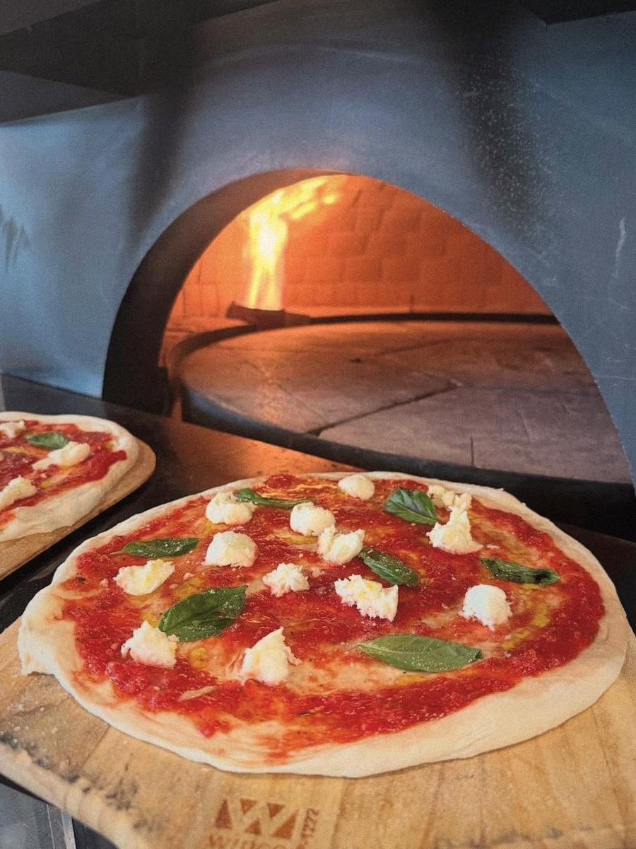 A Margherita on a wooden peel at the mouth of the oven