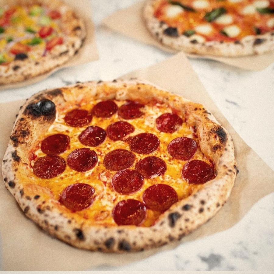 A pepperoni pizza fresh out of the oven, with more pizzas behind it