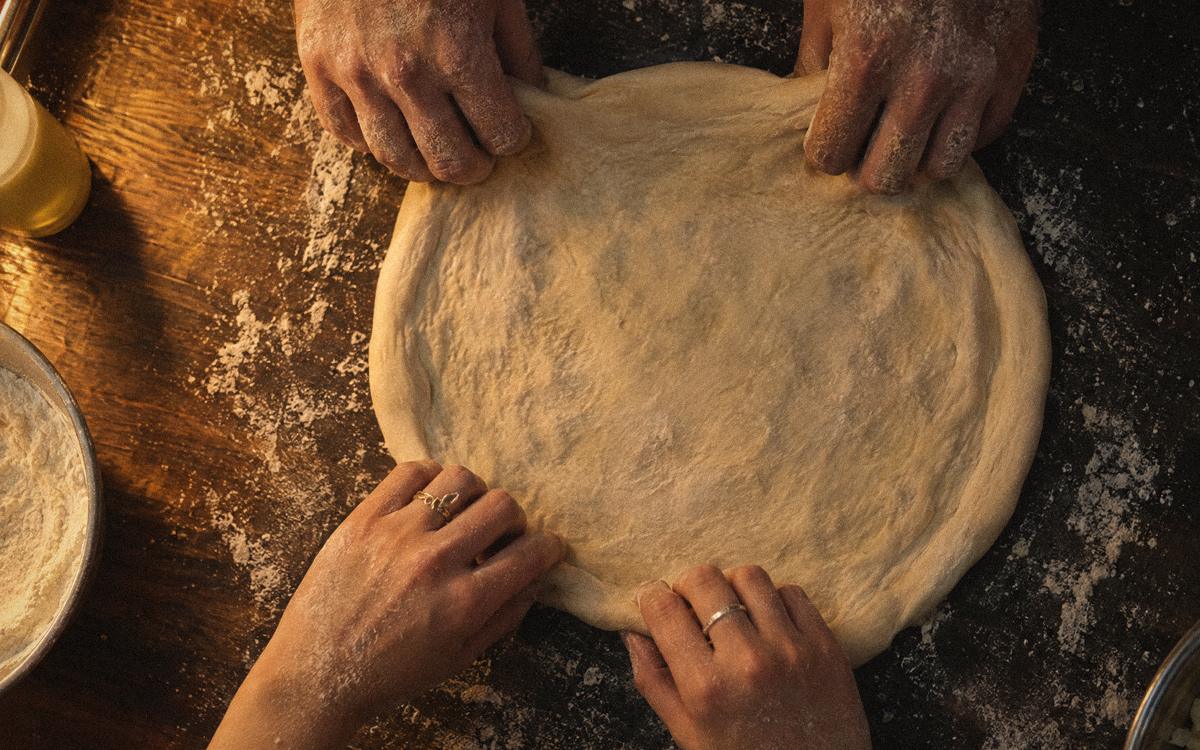 Two pairs of hands stretching one round of dough together